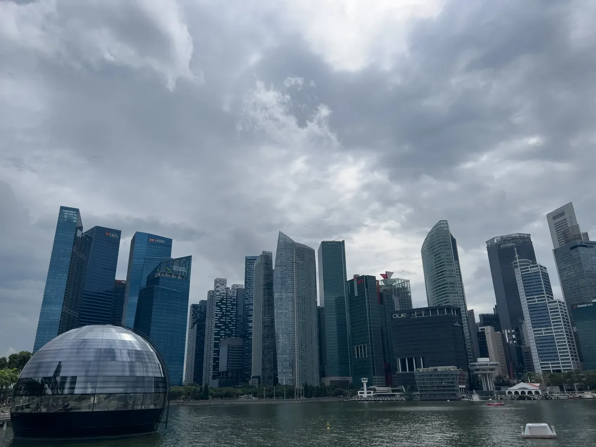 In the Civic District, Downtown Core, Central Region, Singapore, an impressive skyline unfolds. Tall, modern skyscrapers of glass and steel rise majestically into the sky while a silver, dome-shaped structure floats on the water in the foreground. An overcast sky gives the scene a dramatic atmosphere. The water mirrors the architecture, creating a harmonious link between nature and urban life.